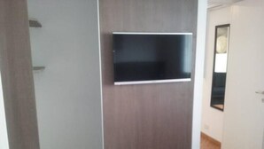 Ett rum med en garderob i trä, en platt-TV som är monterad på väggen och ett trägolv.