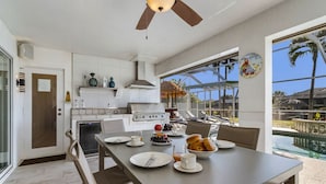 A modern kitchen with a dining area, large windows, and a view of a pool. - Villa Palm Garden heated Pool (Cape Coral)