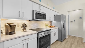 A modern kitchen with white cabinets, a stainless steel refrigerator, a microwave, and a coffee maker. - Villa Palm Garden heated Pool (Cape Coral)