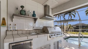 A modern kitchen with a built-in grill, a stainless steel refrigerator, and a poolside view. - Villa Palm Garden heated Pool (Cape Coral)