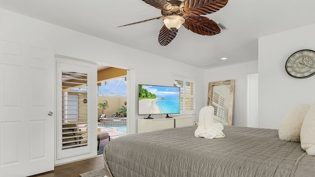 A bedroom with a large bed, a ceiling fan, a TV, and a view of a pool and outdoor area. - Villa Tuscany: Luxury Stay with Pool & Spa (Cape Coral)