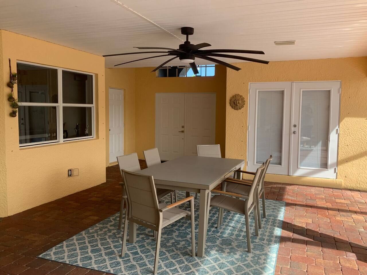 A patio with a table and chairs, a ceiling fan, and a brick floor.