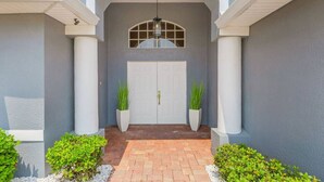 A house entrance with a double door, two potted plants, and a brick pathway. - Villa Tuscany: Luxury Stay with Pool & Spa (Cape Coral)
