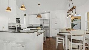 A modern kitchen with white cabinetry, a central island, stainless steel appliances, and pendant lighting. - Villa Tuscany: Luxury Stay with Pool & Spa (Cape Coral)