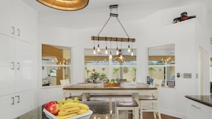 A modern kitchen with white cabinetry, a central island with a fruit bowl, and pendant lighting. - Villa Tuscany: Luxury Stay with Pool & Spa (Cape Coral)