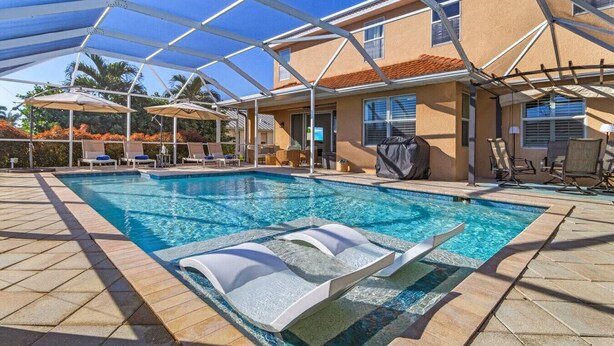 A swimming pool with lounge chairs and umbrellas, surrounded by a covered patio area. - Villa American Beauty (Cape Coral)