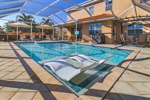 A swimming pool with lounge chairs and umbrellas, surrounded by a covered patio area. - Villa American Beauty (Cape Coral)