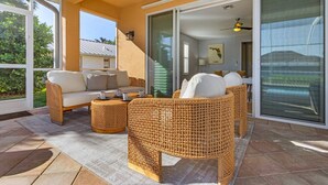 A covered outdoor seating area with wicker furniture and a glass door leading to a room. - Villa American Beauty (Cape Coral)