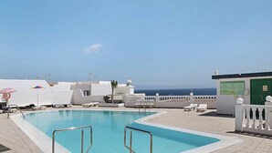 Ein Poolbereich mit Liegestühlen und Sonnenschirmen, mit freiem Blick auf den Ozean, und ein Gebäude mit einer grünen Tür.