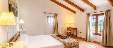 Een slaapkamer met een bed, twee nachtkastjes met lampen, een bureau, een stoel, een raam met gordijnen en een plafondventilator.