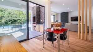 Un salón moderno con una mesa de comedor roja, sillas negras y suelo de madera. Hay una chimenea, un sofá y una televisión al fondo.
