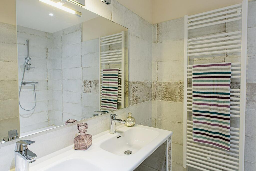 A bathroom with a white sink, a mirror, a shower, and a towel rack with striped towels.