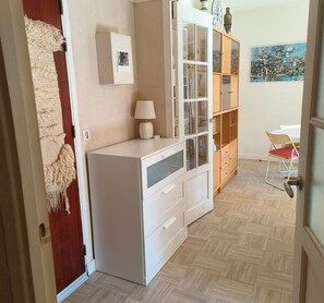 Una habitación con un armario blanco, una lámpara, un mueble de madera con puertas de cristal, una silla roja y un cuadro en la pared.