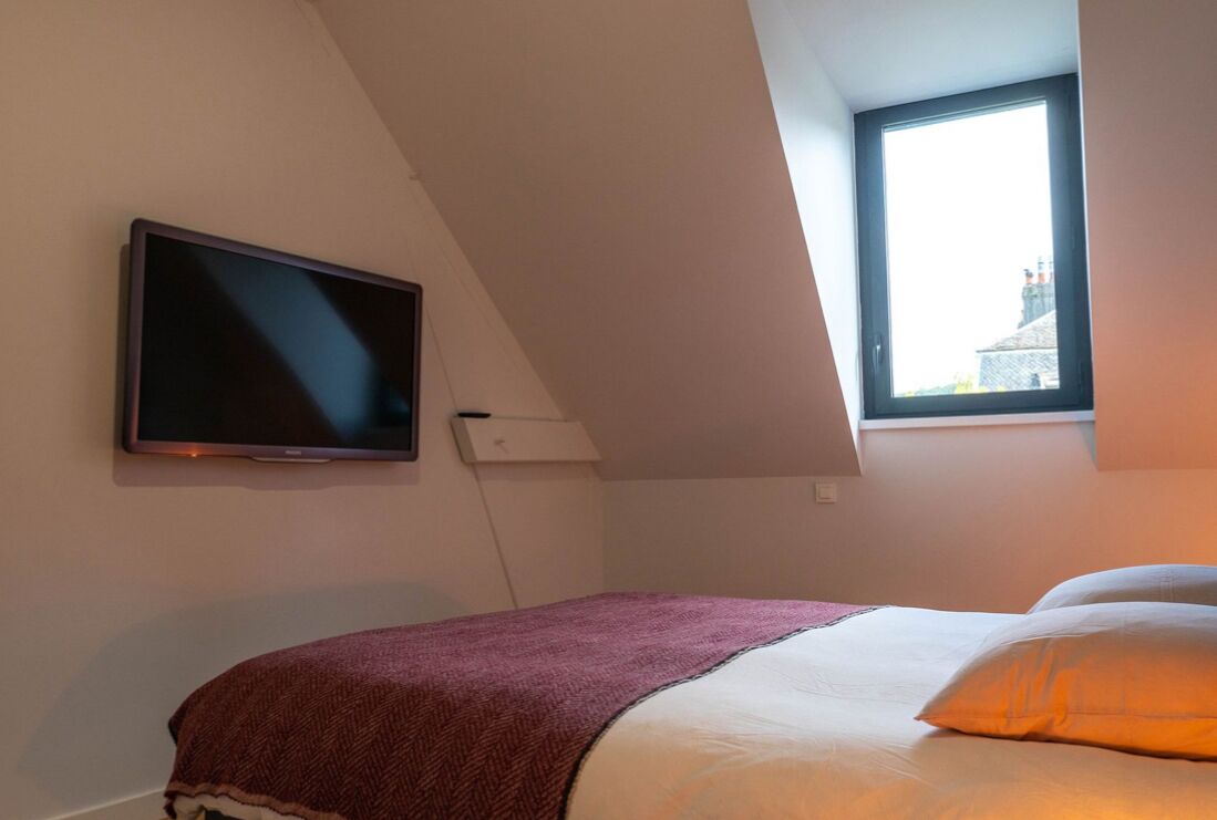 A bedroom with a bed, a television mounted on the wall, and a window providing natural light.