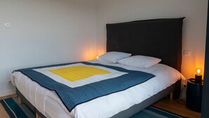 A neatly made bed with a blue and white quilt, a black headboard, and a bedside lamp. - Appartement Spacieux Centre Ville (Espalion)