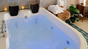 Ein modernes Badezimmer mit einer großen Badewanne, zwei schwarzen Stühlen, einem gewobenen Lampenschirm und einem Holztisch mit Handtüchern.