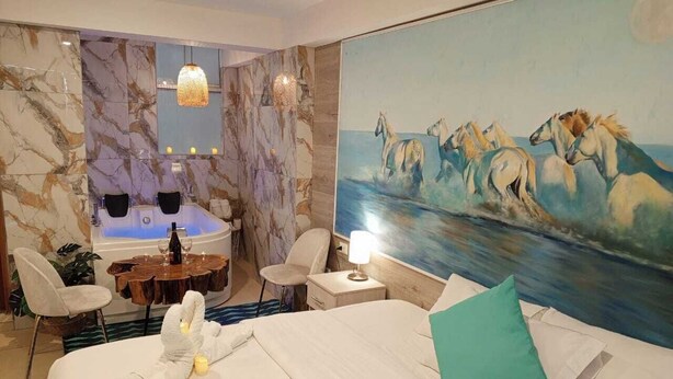 Ein Hotelzimmer mit einem großen Bett, einem Gemälde von Pferden, einer Hydromassage-Badewanne und einer Essecke mit Tisch und Stühlen.