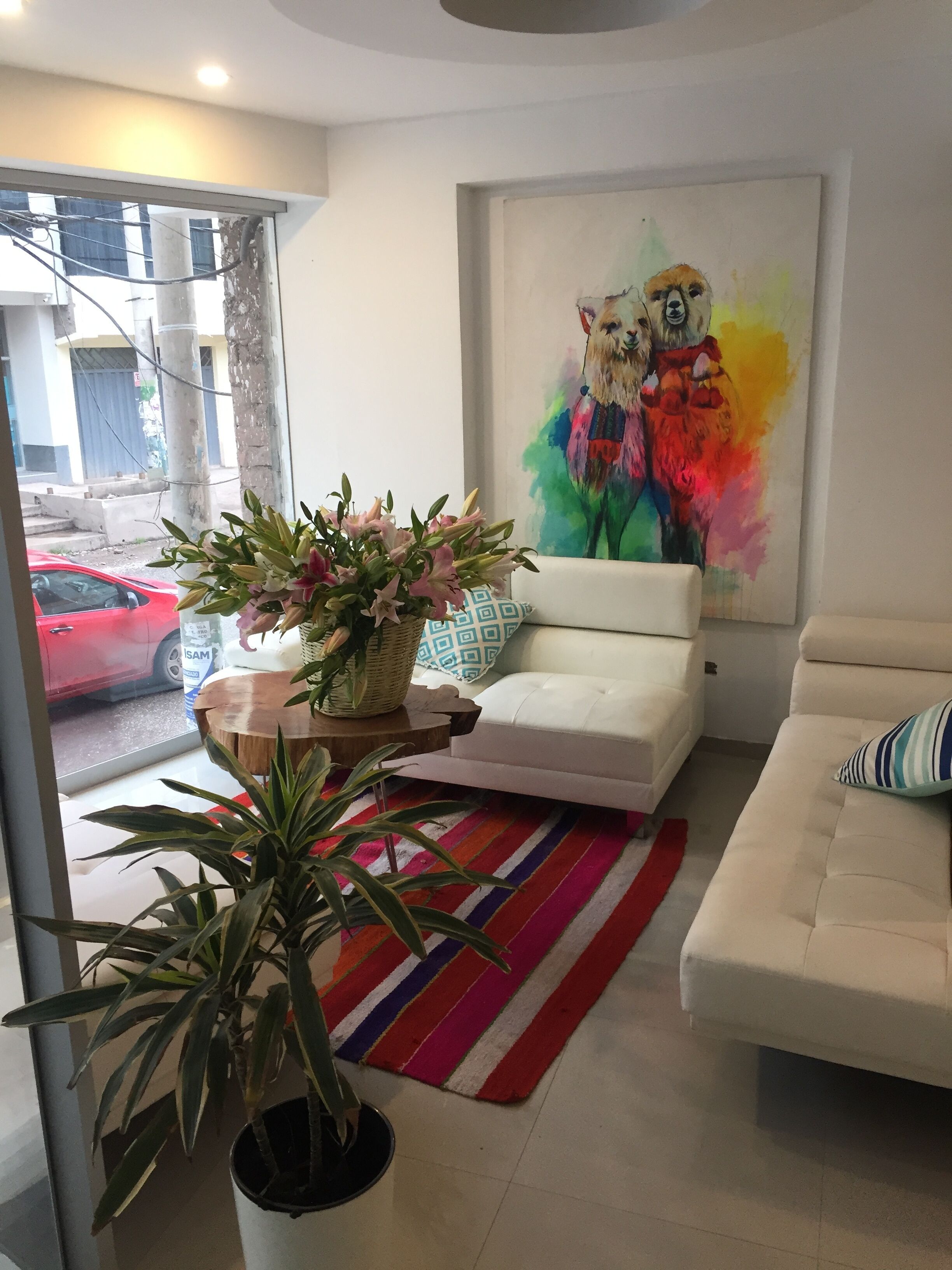 A modern living room with a white sofa, a colorful striped rug, and a large painting of llamas.