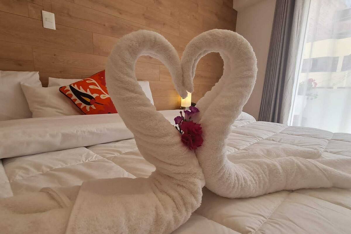 A bed with a heart-shaped towel arrangement and a small flower.