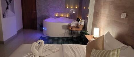 Un dormitorio moderno con una cama grande, una mesita con toallas, una bañera y un espejo.