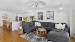 A modern living room with a grey sectional sofa, a round coffee table, and a dining area with a white island and bar stools.