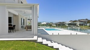 A modern house with a swimming pool, outdoor seating, and a view of neighboring houses.