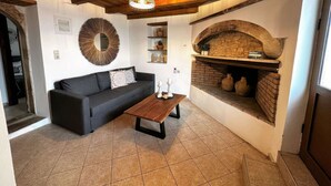 A cozy living room with a dark sofa, a wooden coffee table, a fireplace, and a ceiling light fixture. - Afroditi,2 bedrooms,pool,Margarites,Rethymno,Crete (Pigouniana)