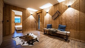 Un intérieur en bois avec un banc, un tapis en fourrure et un lit à l’arrière-plan.