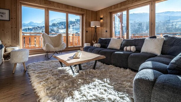 Un salon chaleureux avec une grande fenêtre, un tapis moelleux, un canapé et un fauteuil.