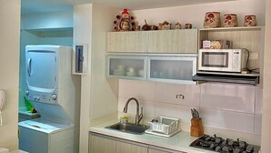 A compact kitchen with a microwave, stove, sink, and a small cabinet.