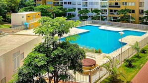 A high-rise residential building with multiple balconies, a swimming pool, and surrounding greenery.