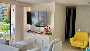 A modern living room with a flat-screen TV, grey sofas, a yellow armchair, and a blue armchair.
