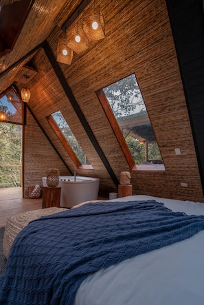 Un dormitorio con una cama grande, una bañera y vistas a árboles por una ventana.
