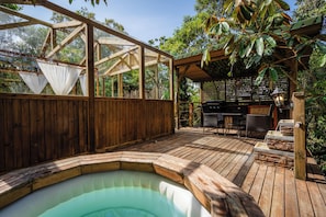 Terraza de madera con jacuzzi, mobiliario exterior y zona de barbacoa.