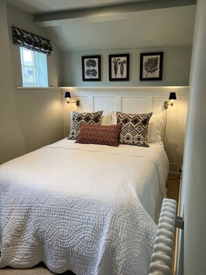 Une chambre à coucher avec un lit, des oreillers, des lampes fixées au mur et des œuvres d’art encadrées accrochées au mur.