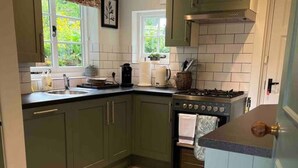 A kitchen with green cabinets, a tiled floor, a stove, and a window with a view of greenery. - Luxury Cottage with Garden (Tewkesbury)