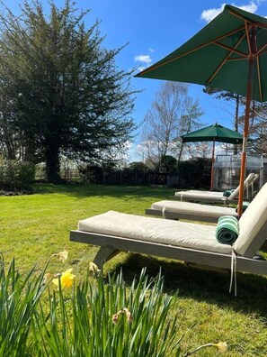 Un espace extérieur verdoyant, aménagé avec des chaises longues et des parasols.