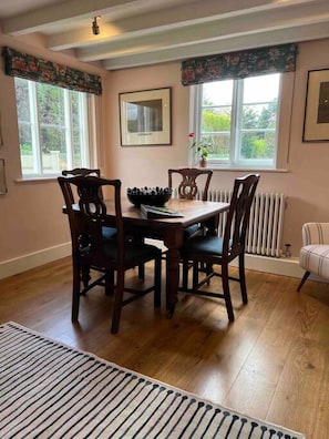 A dining room with a wooden table and chairs, a radiator, and a window with a view of greenery.