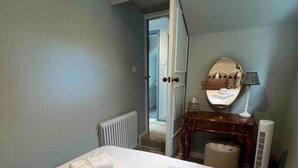 A hotel room with a bed, a bedside table with a lamp, a mirror, and a radiator. - Luxury Cottage with Garden (Tewkesbury)