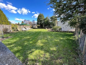 A well-maintained grassy backyard with a wooden fence, a small shed, and a house in the background.