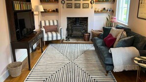 A cozy living room with a fireplace, a sofa, a television, and a bookshelf. - Luxury Cottage with Garden (Tewkesbury)