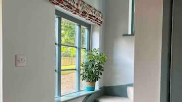 Una escalera con una planta en el rellano, una ventana con un adornos estampados y una puerta a la derecha.