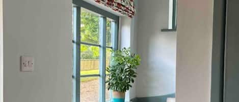 A staircase with a potted plant on the landing, a window with a patterned valance, and a door on the right.
