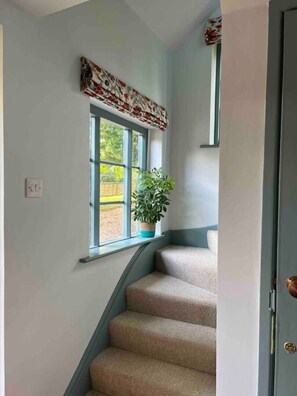 Un escalier dont les marches sont recouvertes d’une moquette beige, menant à un palier doté d’une fenêtre.
