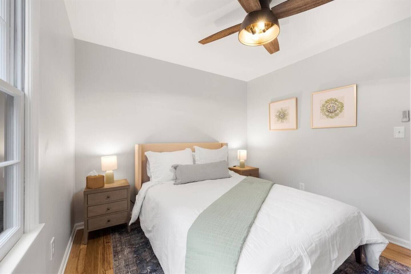 Une chambre à coucher comprenant un lit, des tables de chevet, un ventilateur de plafond et deux cadres photos fixés au mur.