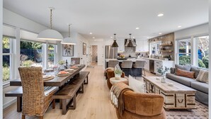Une cuisine spacieuse équipée d’appareils électroménagers modernes, un coin repas avec une longue table et des chaises en osier, et un salon confortable avec un canapé et une table basse.