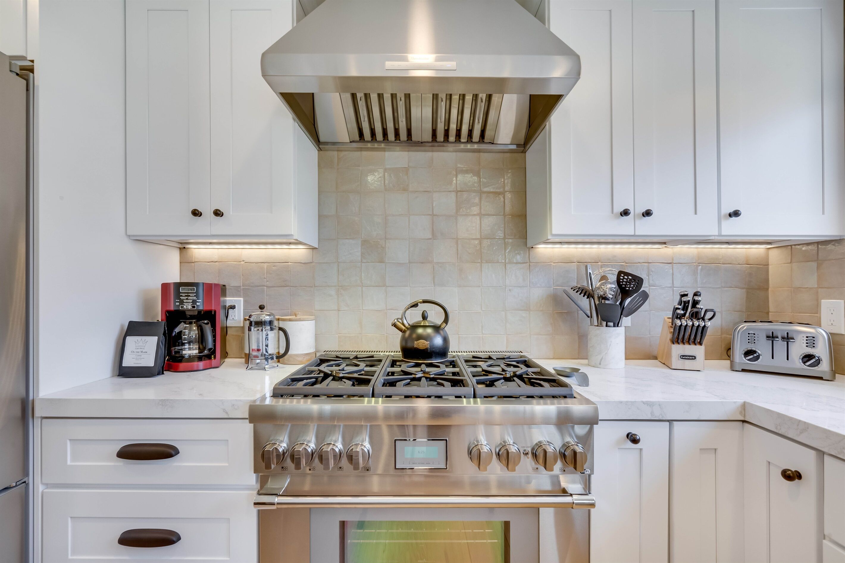 Une cuisine avec des meubles blancs, une cuisinière en acier inoxydable, une machine à café et un grille-pain.
