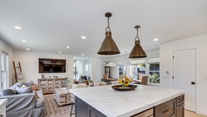 Une cuisine moderne dotée d’un grand îlot central, de luminaires suspendus et d’un coin repas avec un canapé et une table basse.