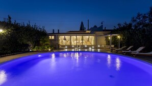 A swimming pool with a blue tint, a covered outdoor seating area, and a building with a covered patio. - Villa Alexandra - Villa with pool (Ispica)