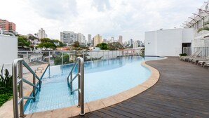 Ein Dachpool mit Holzdeck und Metallgeländern, umgeben von Gebäuden und einer Stadtansicht.